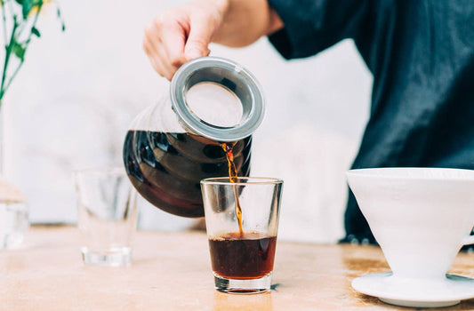 Pouring coffee from a V60 Hario glass coffee server into a clear glass.