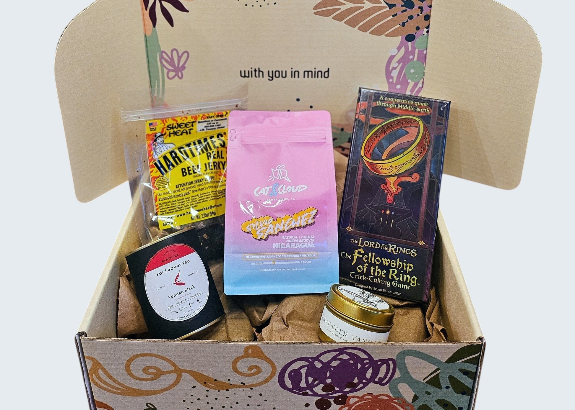 Featured box of the month with fellowship of the ring trick taking game, Cat & Cloud small batch coffee beans, loose leaf black tea, lavender vanilla candle, and hand pressed jerky in sweet heat flavor for a little kick