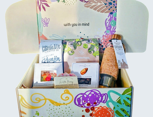Colorful box featuring beautiful and functional tea tumbler with bronze finishings made of quality tempered glass. Jasmine pearls, mixed gummies, milk chocolate almonds, fragrant soap, and quality small batch coffee from award-winning Chromatic Coffee based in San Jose, CA