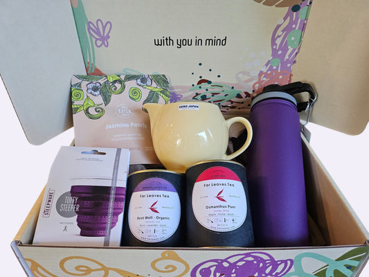 Box containing tea products including a mug, bottles, and boxes with branding.