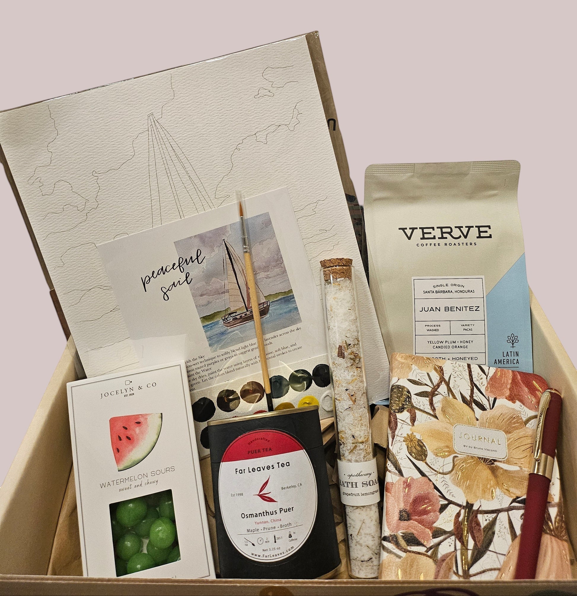 A curated gift box set containing a Verve coffee bag, a watercolor painting book, a notebook with floral illustrations, a small bottle of watercolor paints, and a card reading 'peaceful soul'.